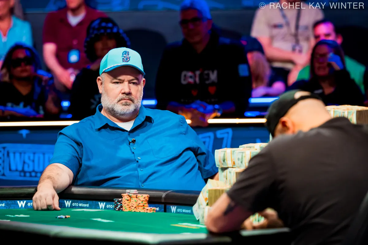 John Wasnock at the 2025 WSOP Main Event final table, focused, wearing a light blue shirt and cap, with large stacks of chips in front of him.
